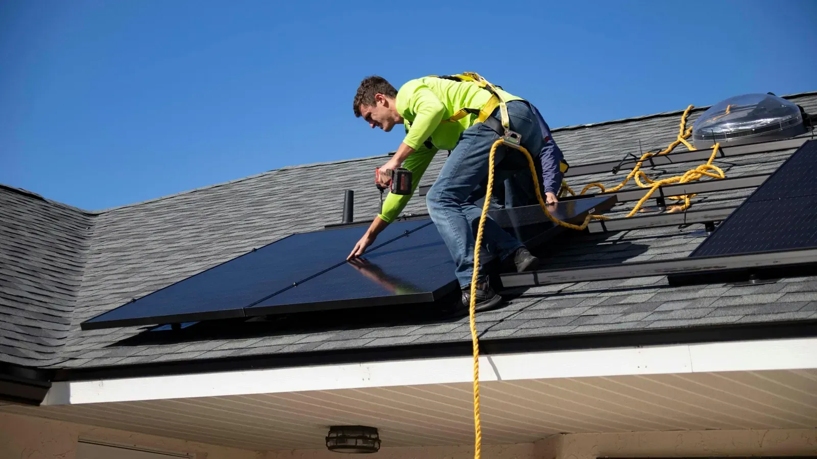 Un installateur, équipé d'un harnais antichute, pose des panneaux photovoltaïques sur une toiture